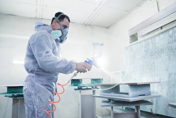 Process of production and manufacture of wooden furniture in factory. Worker man in overalls paints wood with paint spray - Zdjęcie, obraz