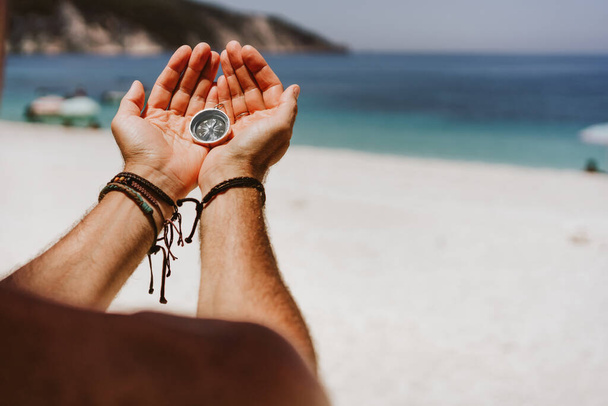 Mans hand holding compass. Beach and sea in background The concept of travel, summer vacation, holiday and journey - Φωτογραφία, εικόνα