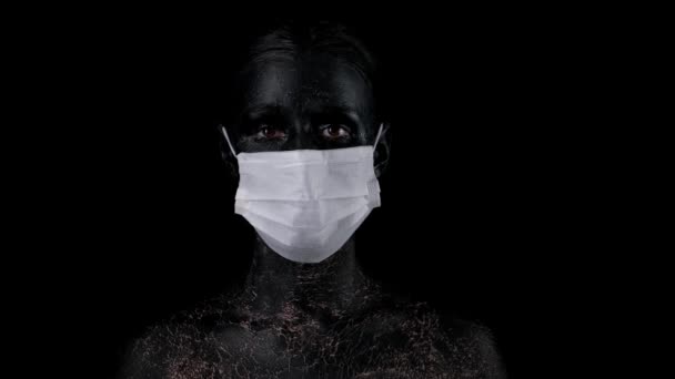 黒色の顔をした女性はコロナウイルスから身を守るために黒い背景に医療用マスクをしている。新しいコロナウイルス2019-nCoV,パンデミック. - 映像、動画