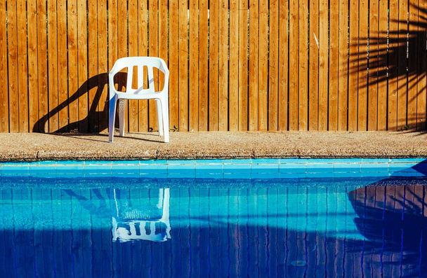 vintage style relaxation pool side space without people here water surface foreground plastic white chair near wooden wall background wallpaper poster picture in summer sunny weather time - Photo, Image