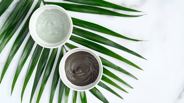 Clay face masks in bowls with tropical palm leaf on marble background, top view. Cosmetic skin rejuvenation treatment, facial skin care concept. - Φωτογραφία, εικόνα