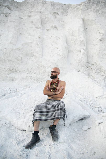 jeune homme avec maquillage primitif et des sorts de perles avec de la poudre dans les mains sur des roches blanches
 - Photo, image