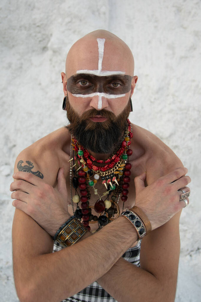 jeune homme avec maquillage primitif et des sorts de perles avec de la poudre dans les mains sur des roches blanches
 - Photo, image