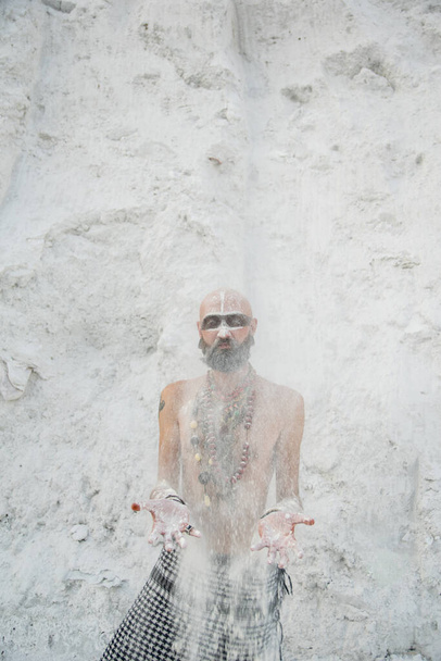 молодий чоловік з первинним макіяжем і бісером заклинання з порошком в руках на білих каменях
 - Фото, зображення