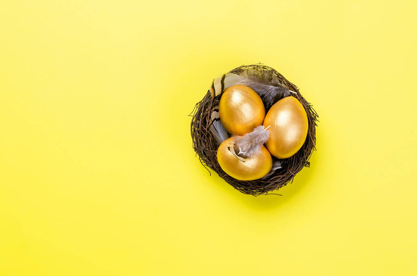 nest with gold decorative eggs and feathers in the nest on a gold background. Spring holiday concept. Copy space, template mockup Easter greeting card with place for text,  - Foto, Imagem
