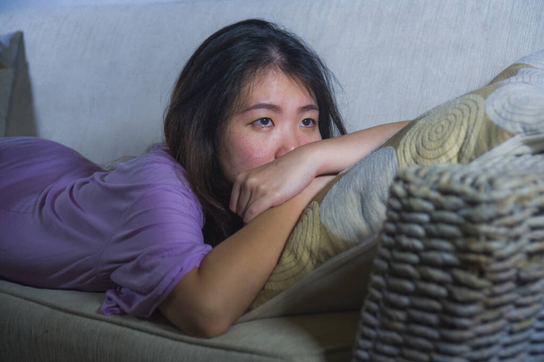 covid-19 virus home lockdown - dramatic portrait of young beautiful depressed and scared Asian Chinese woman lying sad and desperate on sofa couch feeling lonely and in panic about world crisis  - Фото, зображення