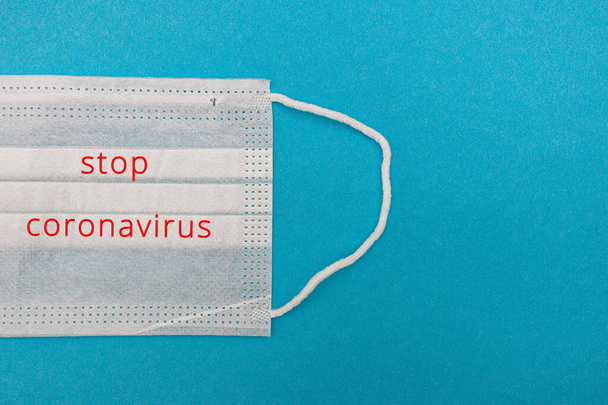 Medical disposable face mask on a blue background with the inscription stop coronavirus covid 19. World pandemic coronavirus. Stop the pandemic. Health and prevention of influenza and an infectious - Valokuva, kuva