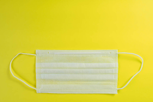 White medical mask on yellow background. Protection against coronavirus, allergies, flu. Surgical mask, top view, copy space - Φωτογραφία, εικόνα