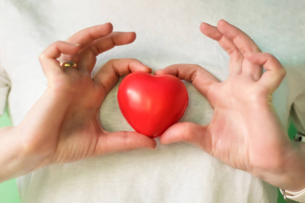Een close-up van handen met een rood hart. Concept voor liefdadigheid, ziektekostenverzekering, liefde, internationale cardiologiedag, hoop, donatie en hulp tijdens coronavirus covid-2019 pandemie. - Foto, afbeelding