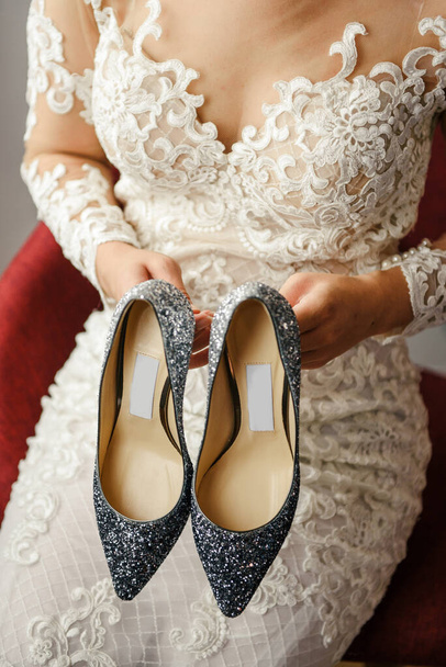 beautiful bride in a lace wedding dress holds stylish gray high-heeled shoes from a famous brand - Photo, Image