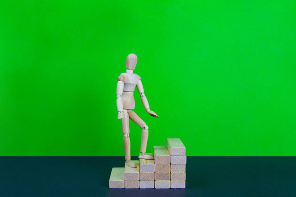 Wooden man walk up the career stairs. Ladder made with wooden bricks. Mannequin on top of development. Concept of personal development, career , changes, success. Green background, copy space for ad. - Fotografie, Obrázek