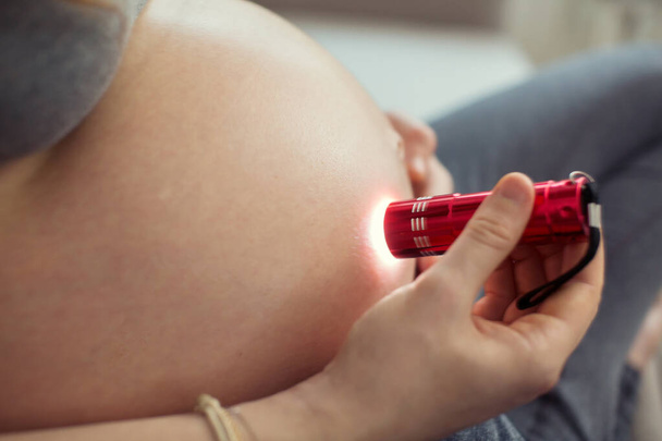 Pregnant woman using flashlight on a belly. Pregnancy flashlight.  - Zdjęcie, obraz