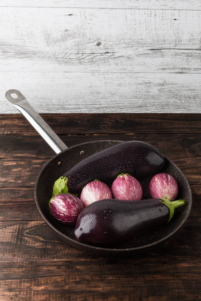 Wet eggplants in frying pan on rustic wooden table. Vertical image with copy space - Foto, Bild