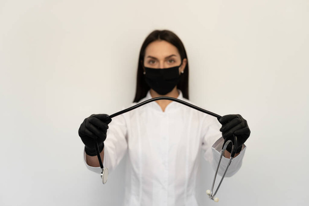 Жінка-лікар у чорній захисній медичній масці та чорних рукавичках, стетоскоп на шиї
 - Фото, зображення