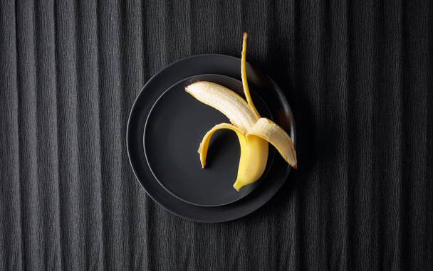 Dojrzały soczysty banan na czarnym talerzu. Widok z góry, przestrzeń kopiowania. - Zdjęcie, obraz