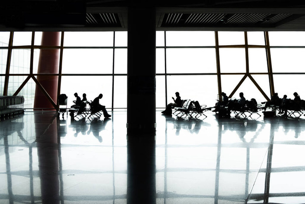 People silhouettes sitting in Airport terminal near large window with reflections - Photo, Image