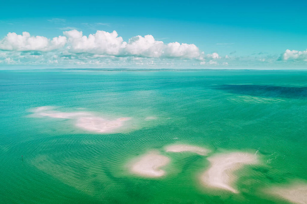 Αεροφωτογραφία των χνουδωτών νεφών πάνω από ζωηρά γαλαζοπράσινα ρηχά νερά του ωκεανού και κηλίδες άμμου - Φωτογραφία, εικόνα