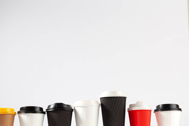 Fila de tazas de café en blanco de plástico con tapas de varios tamaños y colores sobre fondo blanco con espacio de copia
 - Foto, imagen