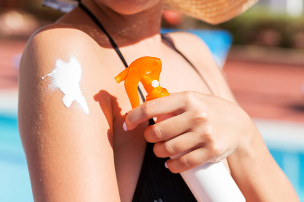 Blanke vrouw die zonnecrème op haar schouder legt bij het zwembad onder de zon op zomerdag. Sun Protection Factor in vakantie, concept. - Foto, afbeelding