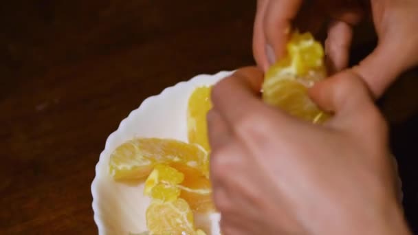 Ręce obierają owoce cytrusowe w zwolnionym tempie. Zdrowe jedzenie. Dłonie kobiety obierają mandarynki. Smaczne mandarynki w plasterkach owoców. Sezonowe owoce cytrusowe. Mandarynka pomarańczowa - Materiał filmowy, wideo