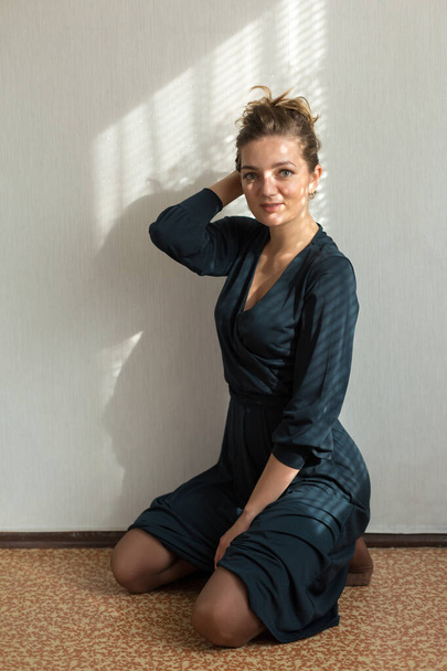 Ritratto di una giovane bella ragazza in una stanza su uno sfondo di un muro grigio con ombre, luce naturale dalla finestra
. - Foto, immagini