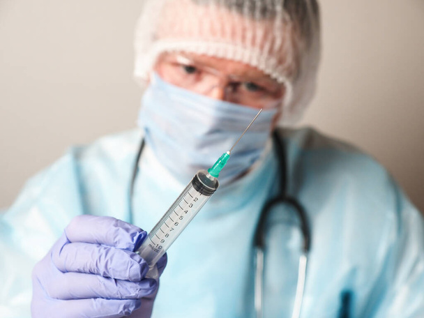 Male Caucasian doctor wearing mask and gloves holds a disposable syringe - Zdjęcie, obraz