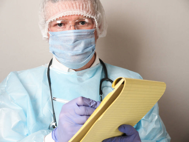 Doctor wearing mask, glases and gloves with a notepad - Foto, Bild