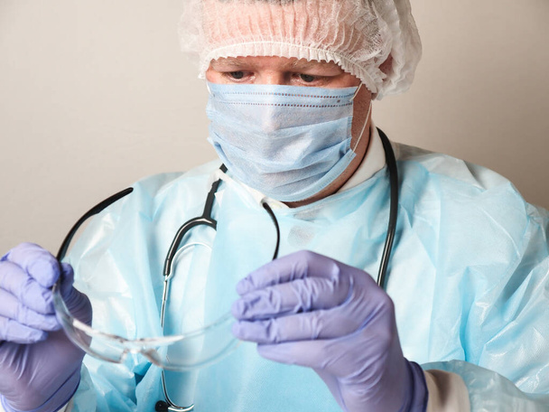 Doctor wearing protective gear checks his protective glasses - Foto, afbeelding
