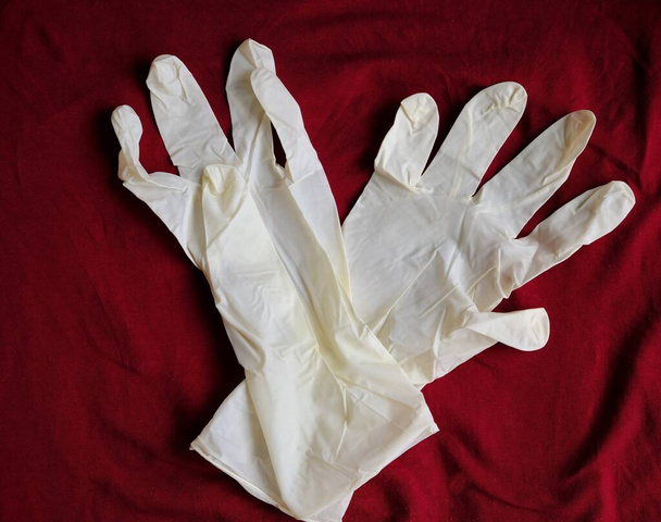Guanti bianchi in lattice su fondo rosso. Protezione delle mani contro infezioni, virus, germi. Isolamento della pelle dal coronavirus
. - Foto, immagini