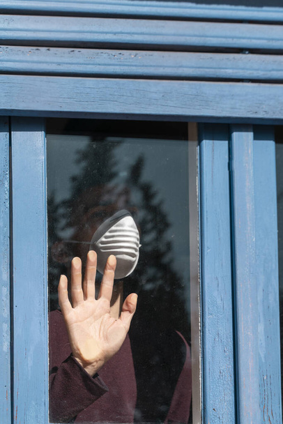Coronavirus. Corona virüsünün hasta adamı pencereden dışarı bakıyor ve maske takıyor ve evdeki hastalıktan korunuyor. Karantinaya alın. Hasta enfeksiyonu önlemek için izole edilmiş. Pandemia. Ev. - Fotoğraf, Görsel