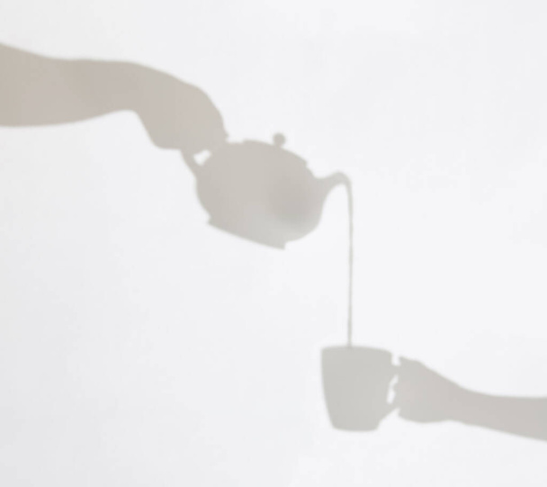 Delicate shadows of teapot pouring liquid into a cup held by female hand. Shadow play. - Фото, зображення