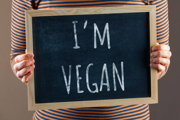Female hands holding small black chalkboard in front of the body with text saying I'm Vegan - Foto, Bild
