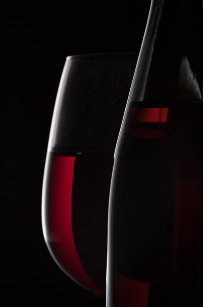 Red wine bottle and wine glass on black background - Фото, зображення
