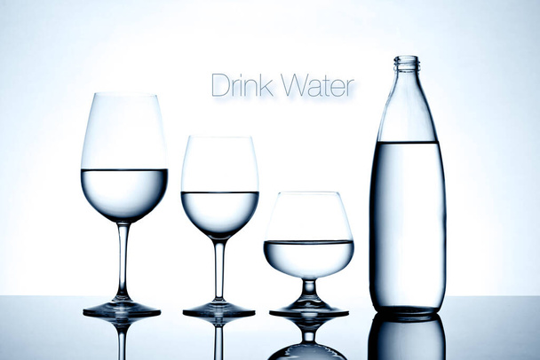 Glassware and bottle filled with water on white background. - 写真・画像