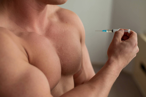 Close-up of a naked male torso. Unrecognizable shirtless bodybuilder man puts himself an injection of testosterone. Faceless athlete takes dope. - Photo, image