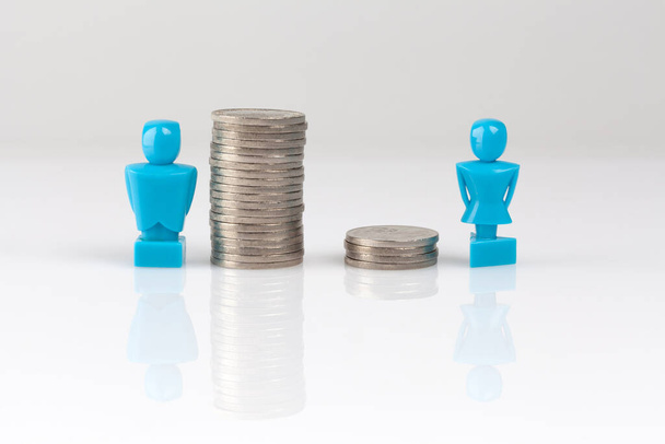 Income inequality concept shown with male and female figurines and piles of coins - Foto, immagini