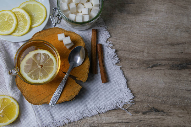Tasse transparente en verre avec thé à la menthe sur un support en bois, à côté d'un bol à sucre avec des cubes de sucre, un citron tranché et une cuillère
. - Photo, image