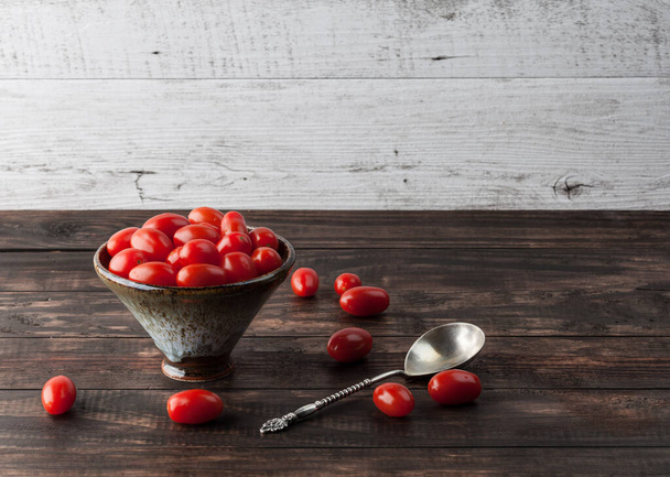 Cherry Roma tomatoes in ceramic bowl on rustic wooden table with vintage spoon. Horizontal image with copy space. - Foto, Imagen