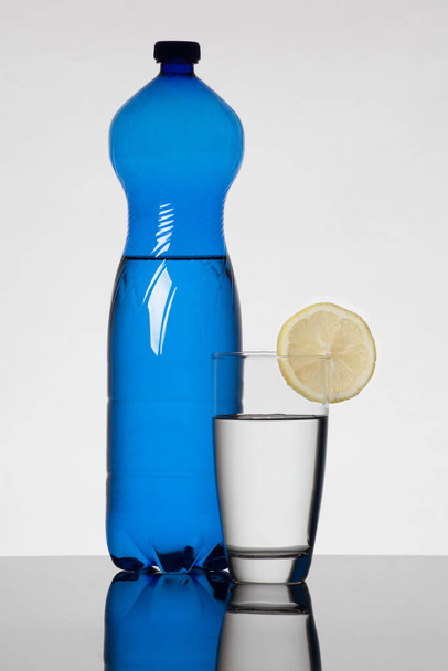 Blue water bottle and glass filled with water and decorated with lemon - 写真・画像