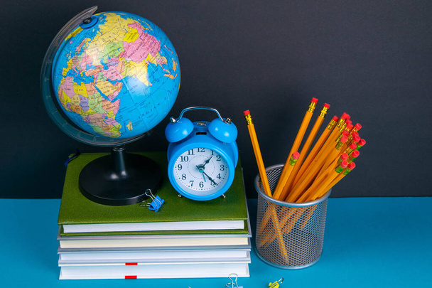 The globe and the clock stand on a stack of books, next to a glass of pencils. - Fotoğraf, Görsel