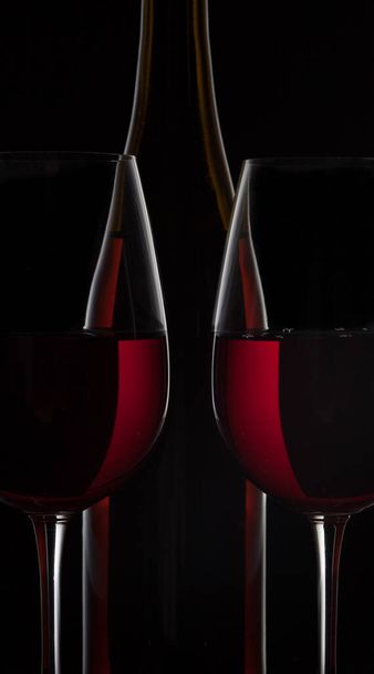 Red wine bottle and two wine glasses on black background - Foto, immagini