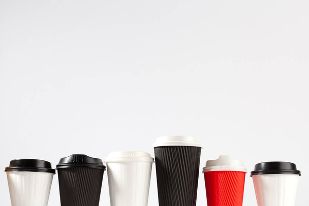 Six disposable blank coffee cups in a row of various sizes and colors with copy space - Foto, imagen