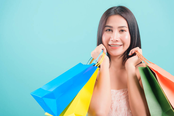 Asijské šťastný portrét krásná mladá žena stojící úsměv v létě nakupování její držení vícebarevné nákupní tašky na ruce a hledá na kameru na modrém pozadí s kopírovat prostor pro text - Fotografie, Obrázek