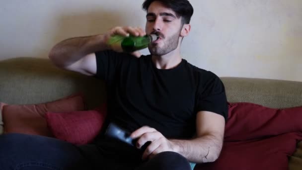 Young man on couch drinking beer and eating - Video