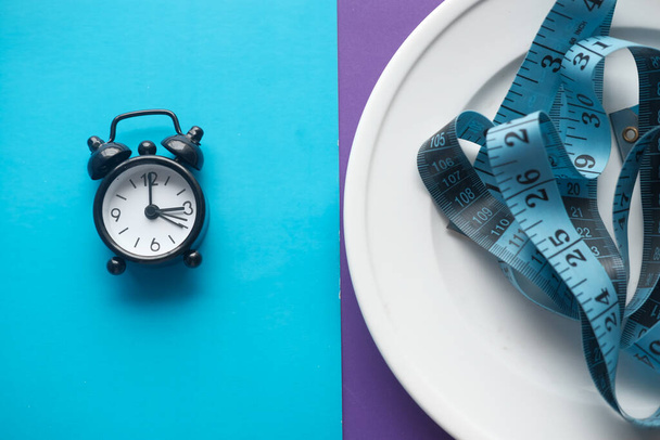 Un orologio su sfondo a colori e metro a nastro, concetto di dieta a digiuno intermittente
 - Foto, immagini