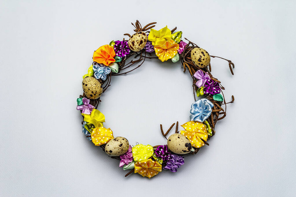 Hand crafted Easter wicker wreath with quail eggs and handmade flowers. Birch branches, polka dot satin ribbon. Stay at home concept. Festive Easter light blue background, top view - Photo, Image