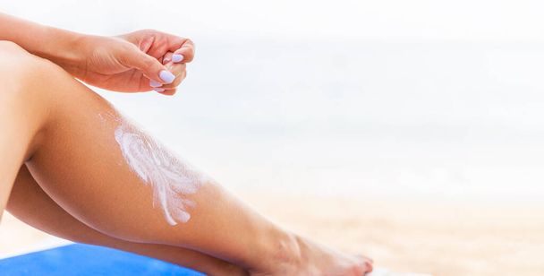 Giovane donna si sta riposando sul lettino in spiaggia e protegge la sua pelle applicando crema solare sulla gamba
. - Foto, immagini