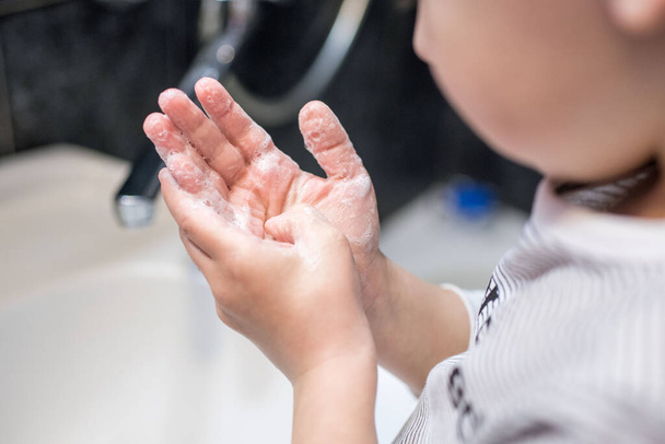 Ein kleiner Junge wäscht sich die Hände mit Seife. Handfärbung durch Viren. - Foto, Bild