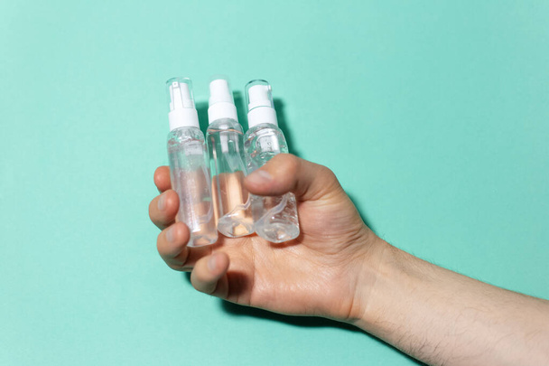 Close-up van mannelijke hand te houden draagbare plastic dispenser flessen met ontsmettingsmiddel antiseptische, antibacteriële gel, coronavirus preventie, geïsoleerd op de achtergrond van cyaan, aqua menthe kleur. - Foto, afbeelding