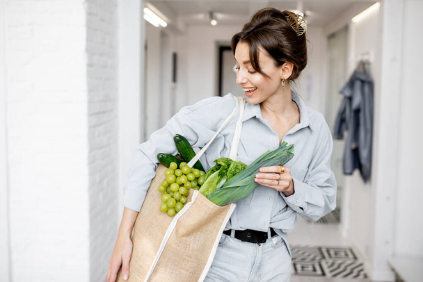 Γυναίκα έρχεται στο σπίτι με τσάντα ψώνια γεμάτη φρέσκα τρόφιμα - Φωτογραφία, εικόνα